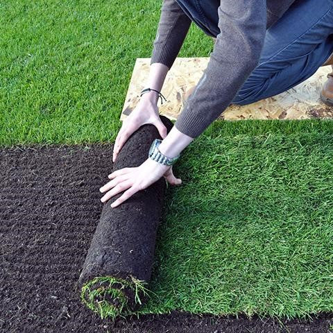 Person rolling out lawn turf while kneeling on a laying board